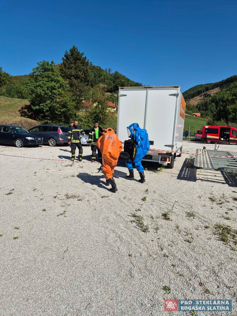 Tekmovalca v oranžni in modri zaščitni obleki prenašata opremo ob tovornem vozilu.